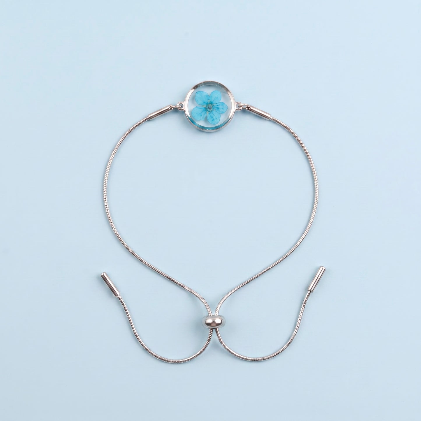 Bracciale scorrevole in acciaio inox e fiore azzurro preservato nel ciondolo